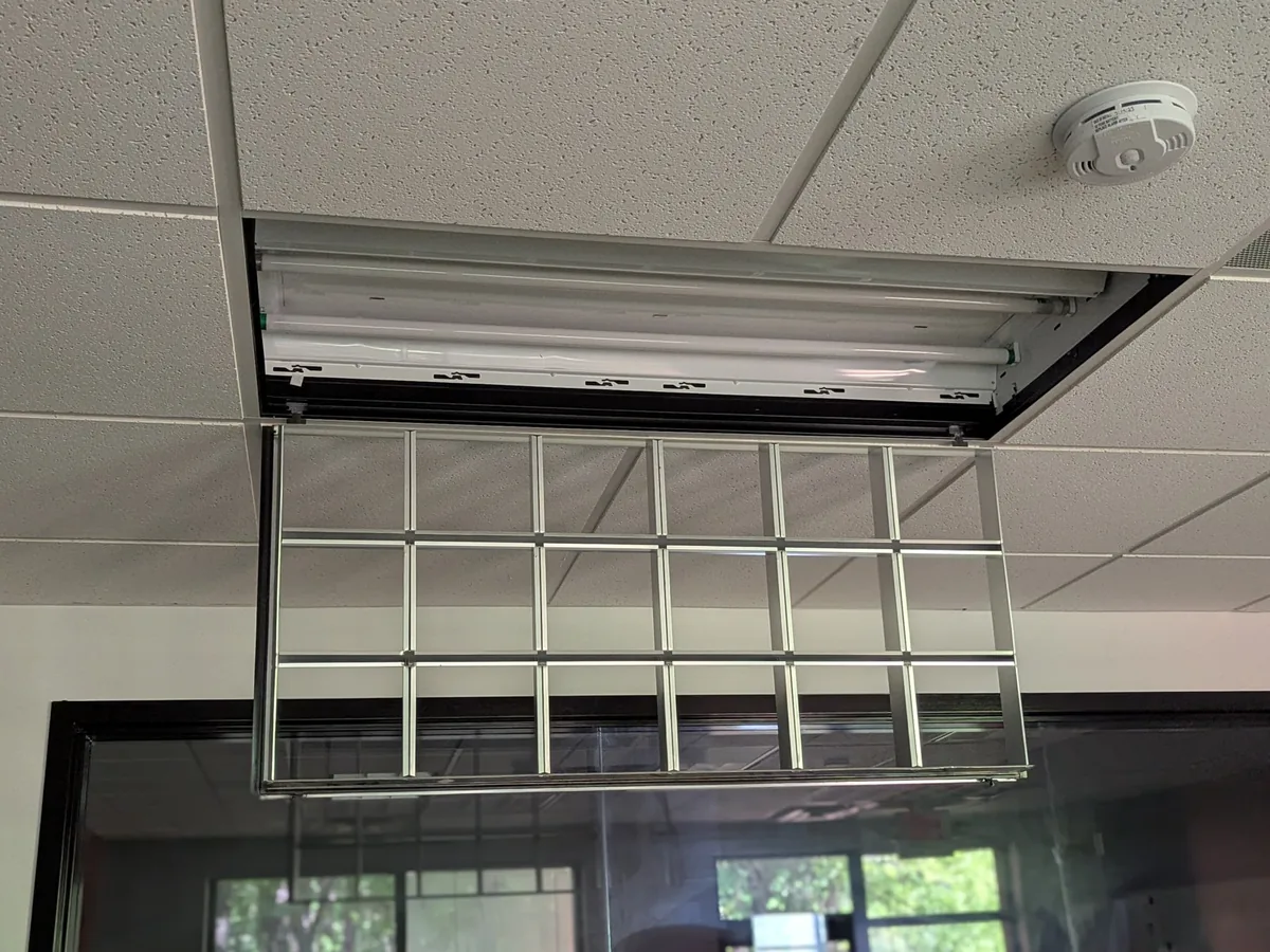 Fluorescent light fixture opened from a drop ceiling, its diffuser grid hanging below
