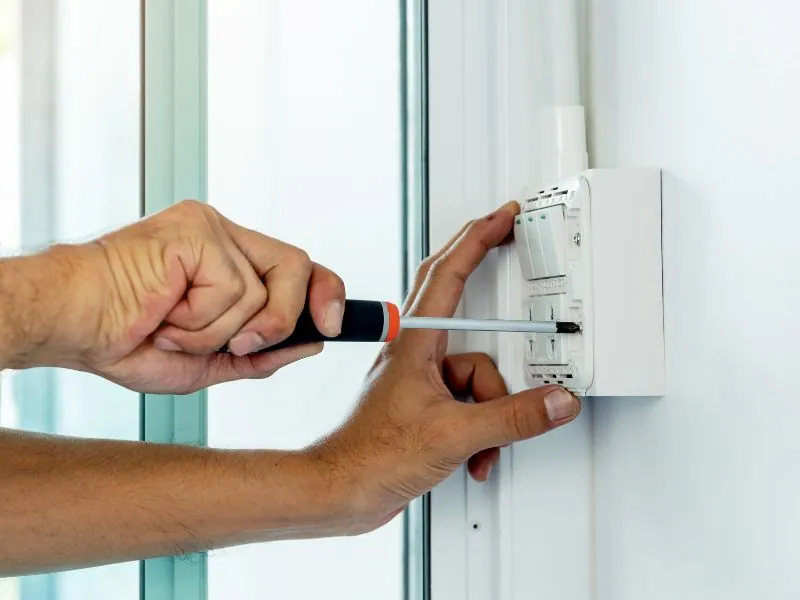 Electrician replacing a wall light switch with a screwdriver