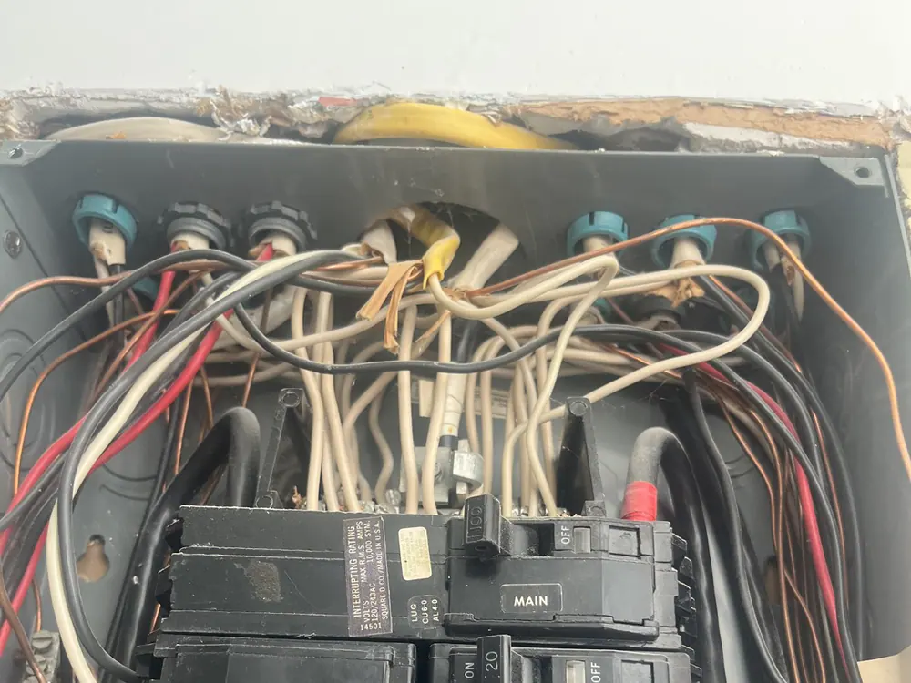 An open electrical panel with a broken cover, showing breakers and a dense mass of wires, in Mordecai, Raleigh