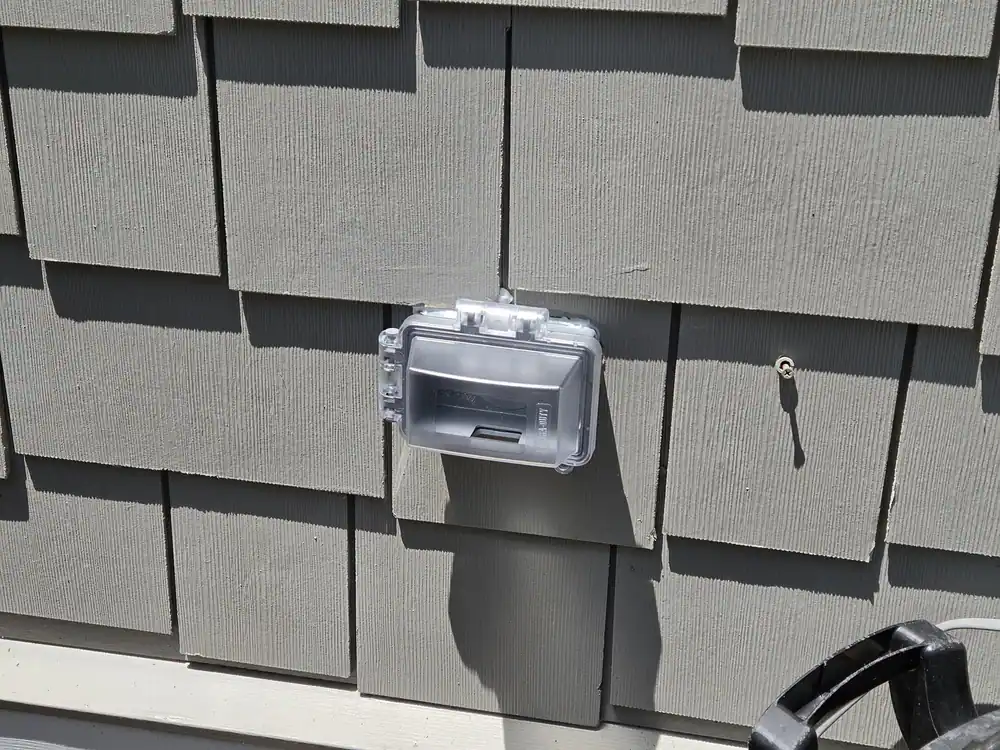 Weatherproof electrical box with a clear plastic cover mounted on gray siding in Cameron Park, Raleigh