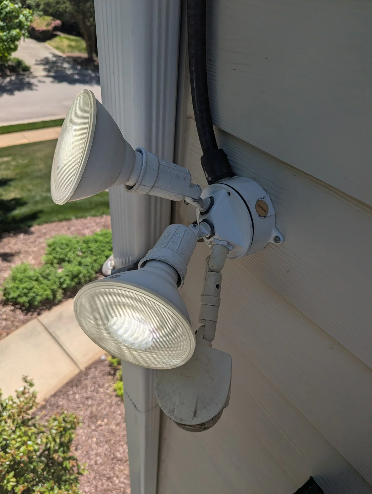 Two outdoor security floodlights mounted on a house wall, one lit and one off, in Budleigh, Raleigh