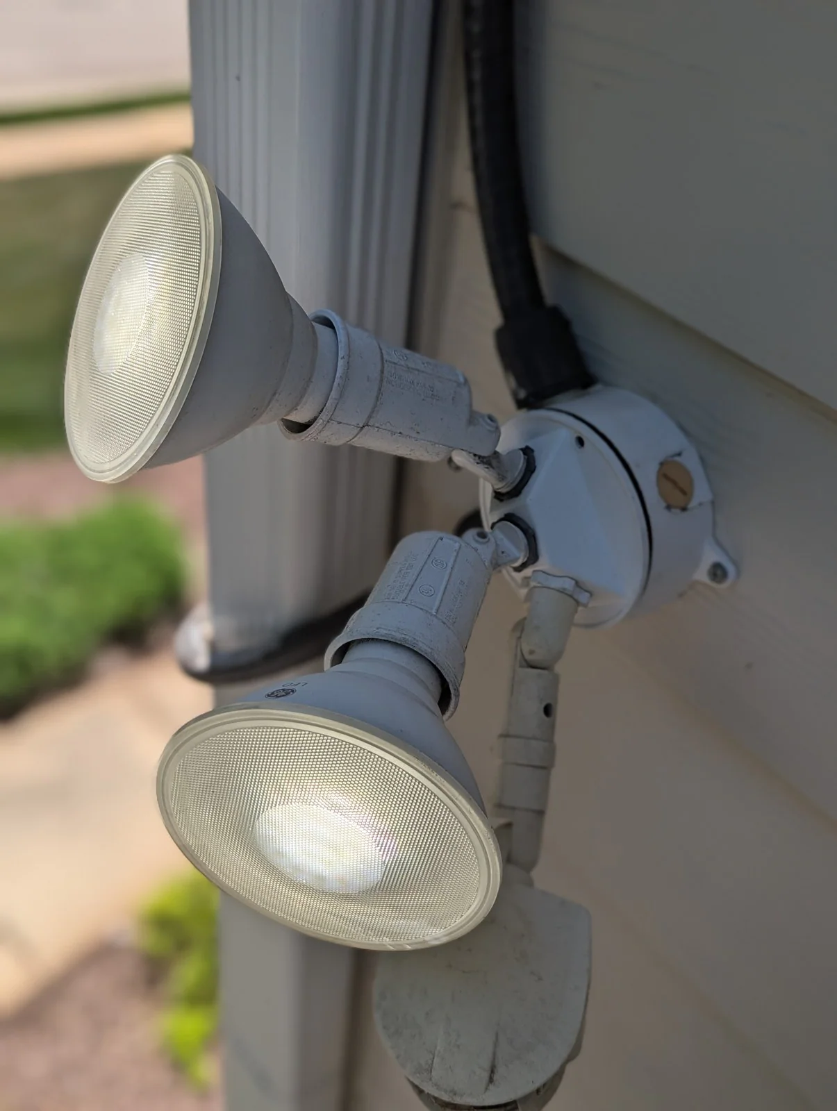 Two outdoor spotlights mounted on a house wall, one lit and one dark, in Budleigh, Raleigh