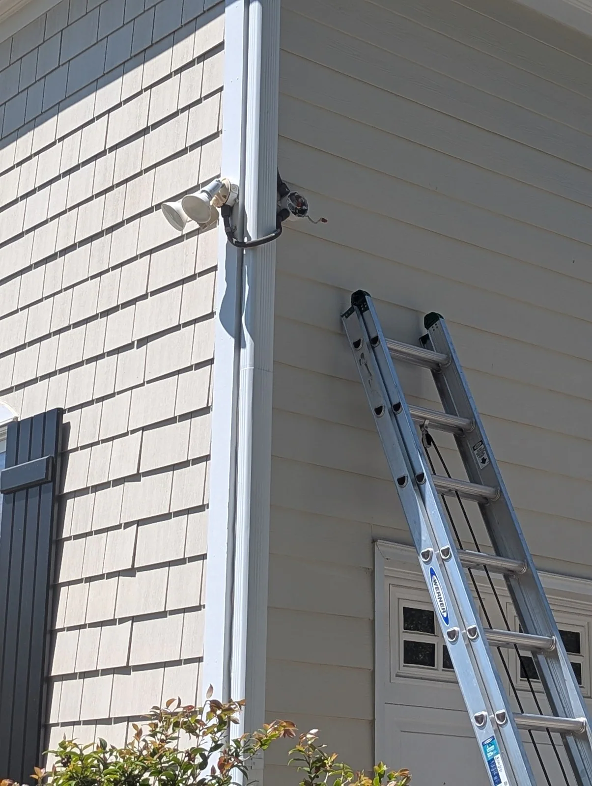 An electrician working on a house exterior near outdoor lighting and a meter mast, with a ladder nearby, in Budleigh, Raleigh