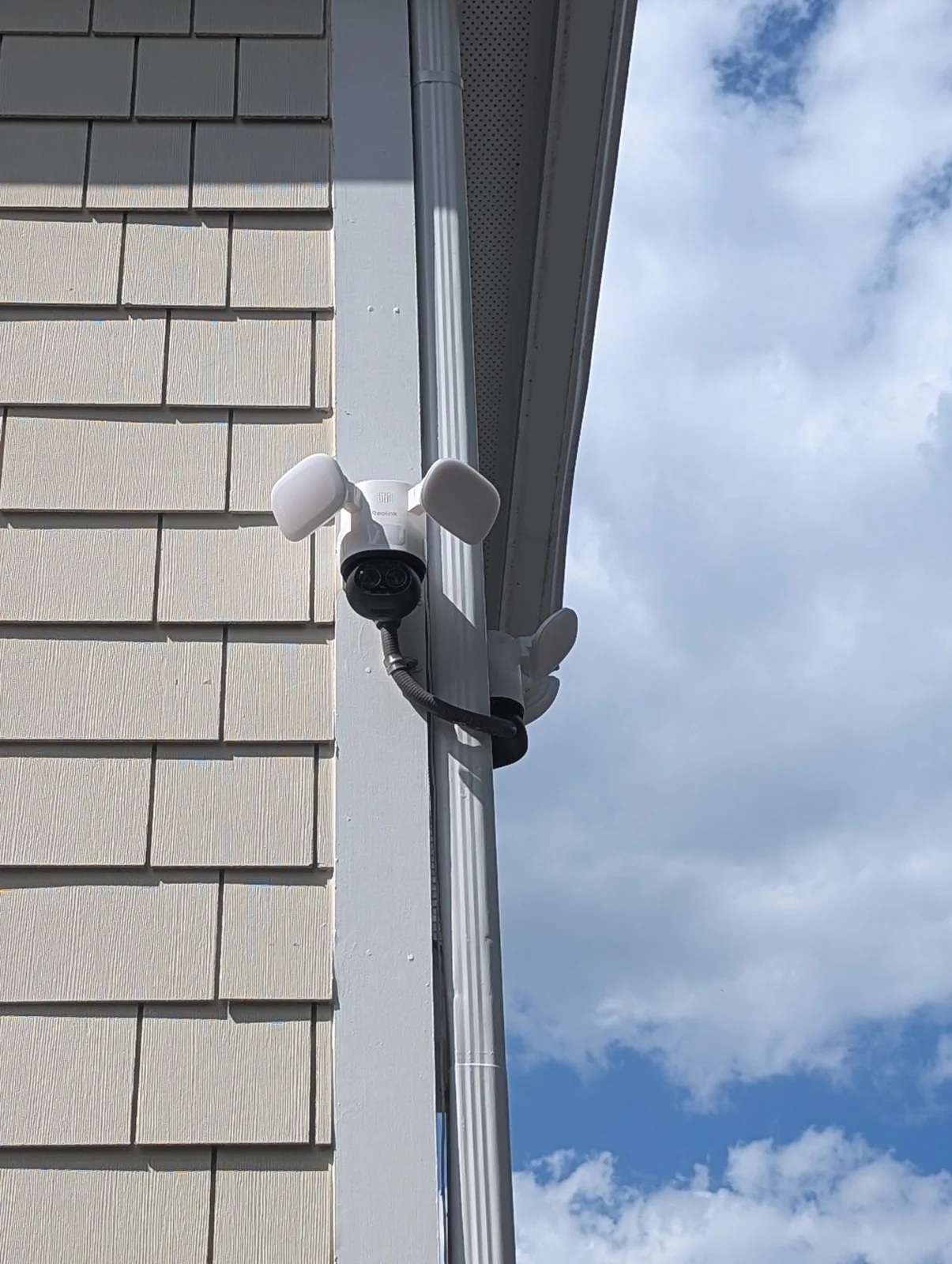 A security camera with lights mounted on a house corner under a cloudy sky, in Budleigh, Raleigh
