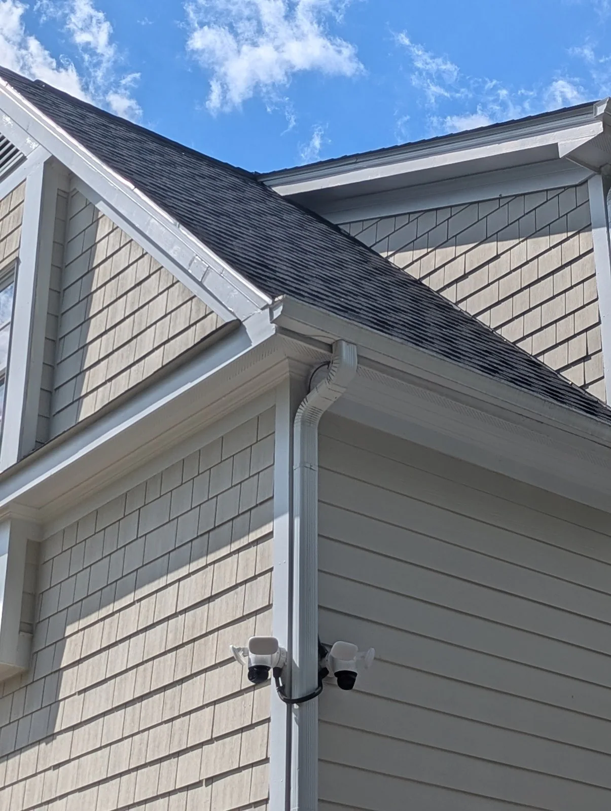 Two security cameras mounted near a downspout on a house under a clear sky, in Budleigh, Raleigh
