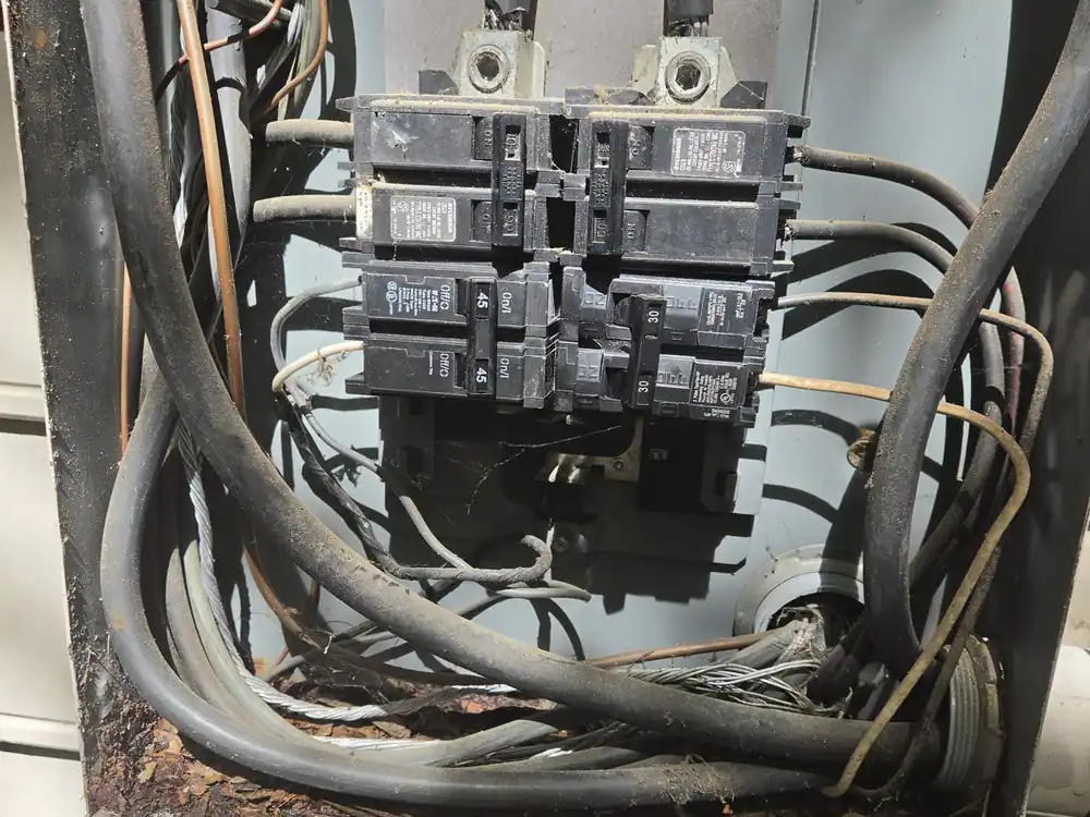 A dirty, cluttered electrical panel with exposed wires and rusted metal, in Oakwood, Raleigh