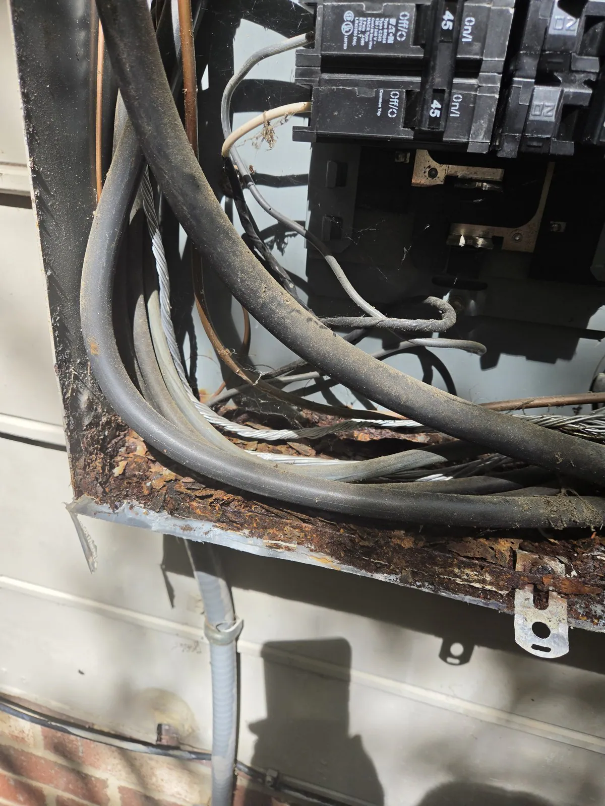 A rusted electrical panel with tangled wires and a broken metal frame, mounted outdoors, in Oakwood, Raleigh