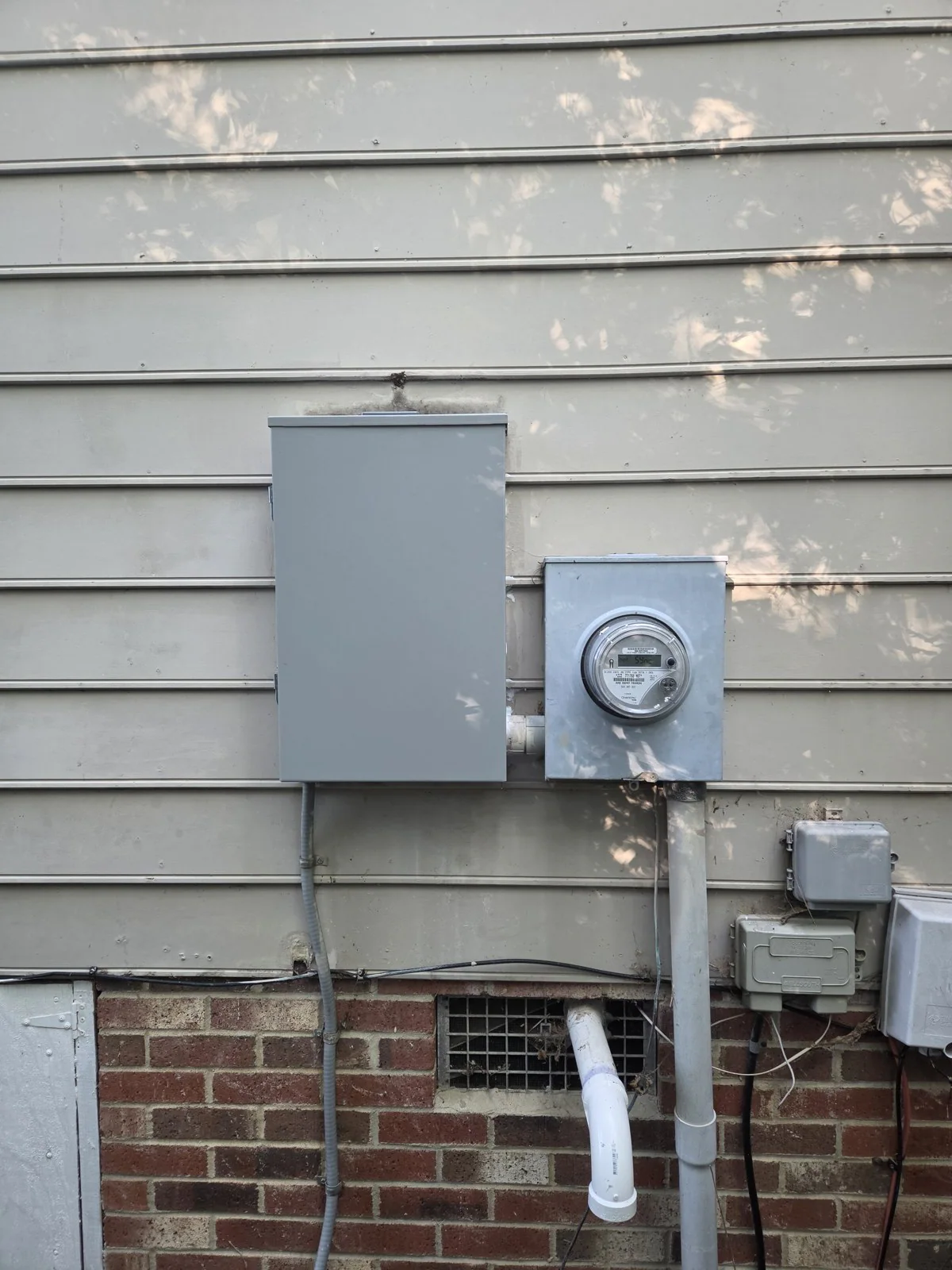 A utility meter and an electrical panel mounted on the exterior wall of a house, in Oakwood, Raleigh