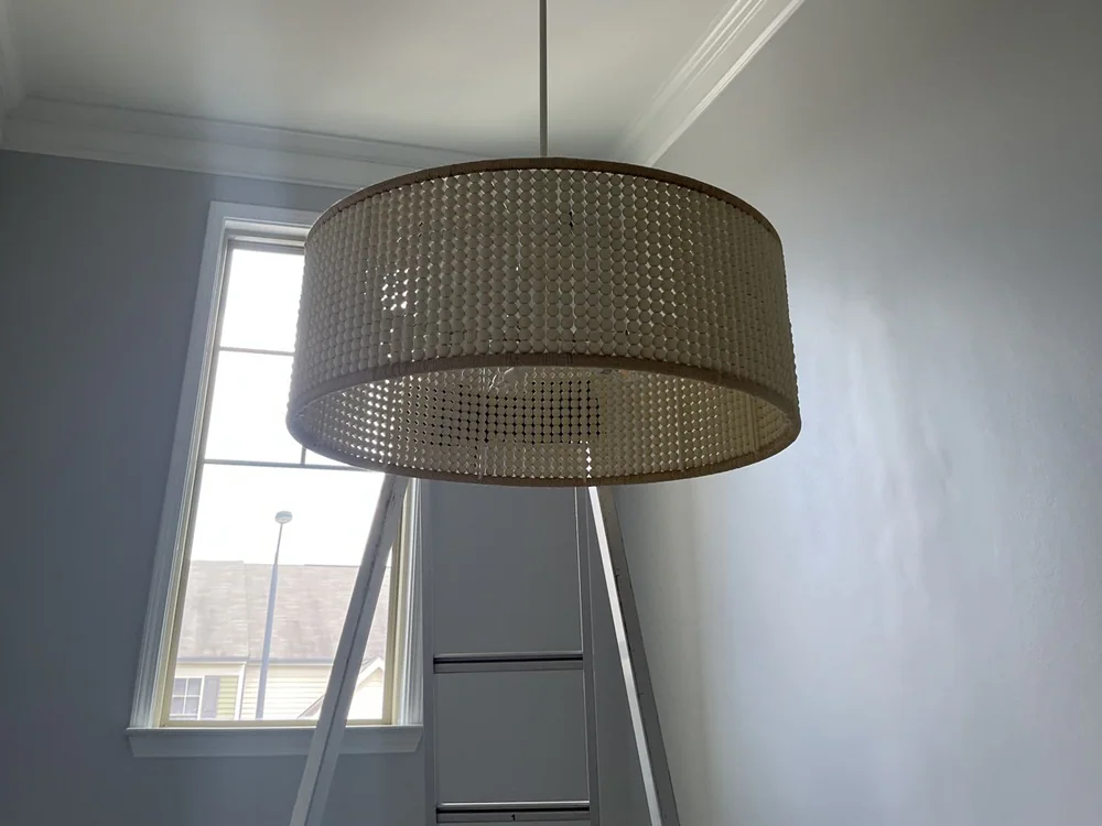 A woven pendant light fixture hanging from a high ceiling, with a ladder below, in Ridgewood, Raleigh