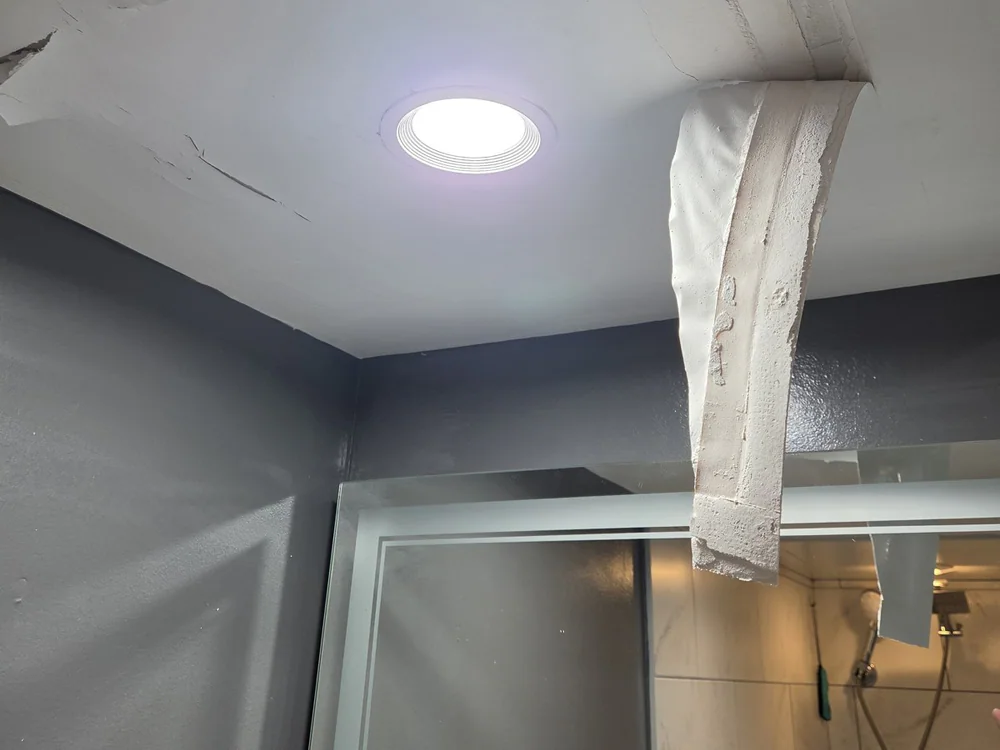 A ceiling with torn and water-stained drywall surrounding a recessed light fixture, photographed during the repair, in Mordecai, Raleigh