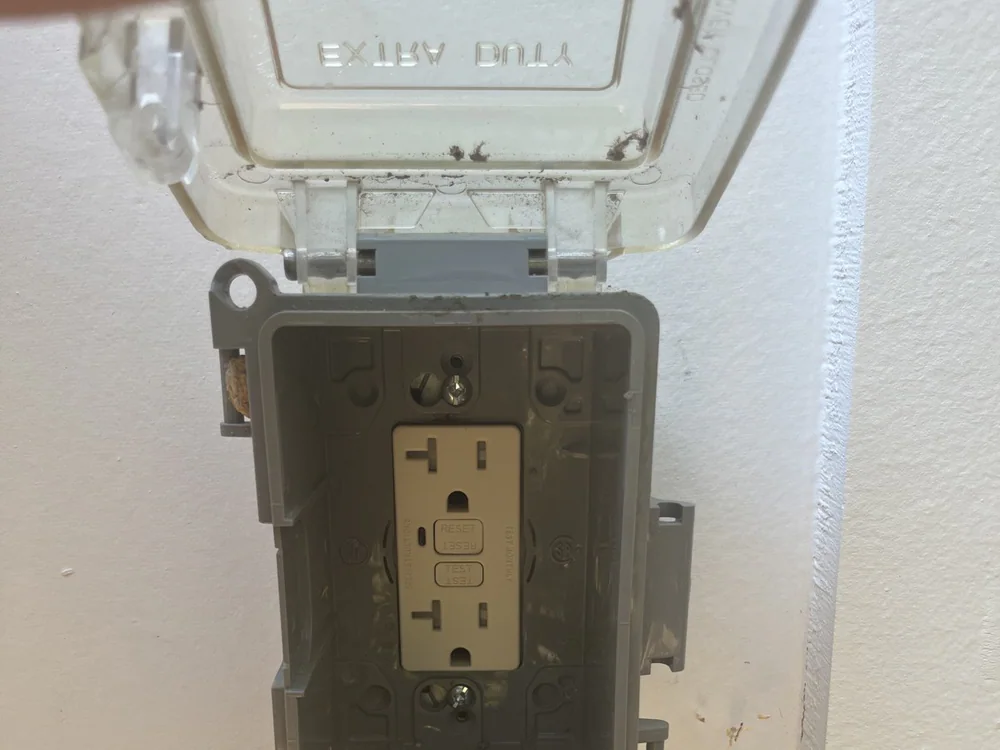 An outdoor outlet with its cover open, showing the reset and test buttons, mounted on an exterior wall, in Laurel Hills, Raleigh