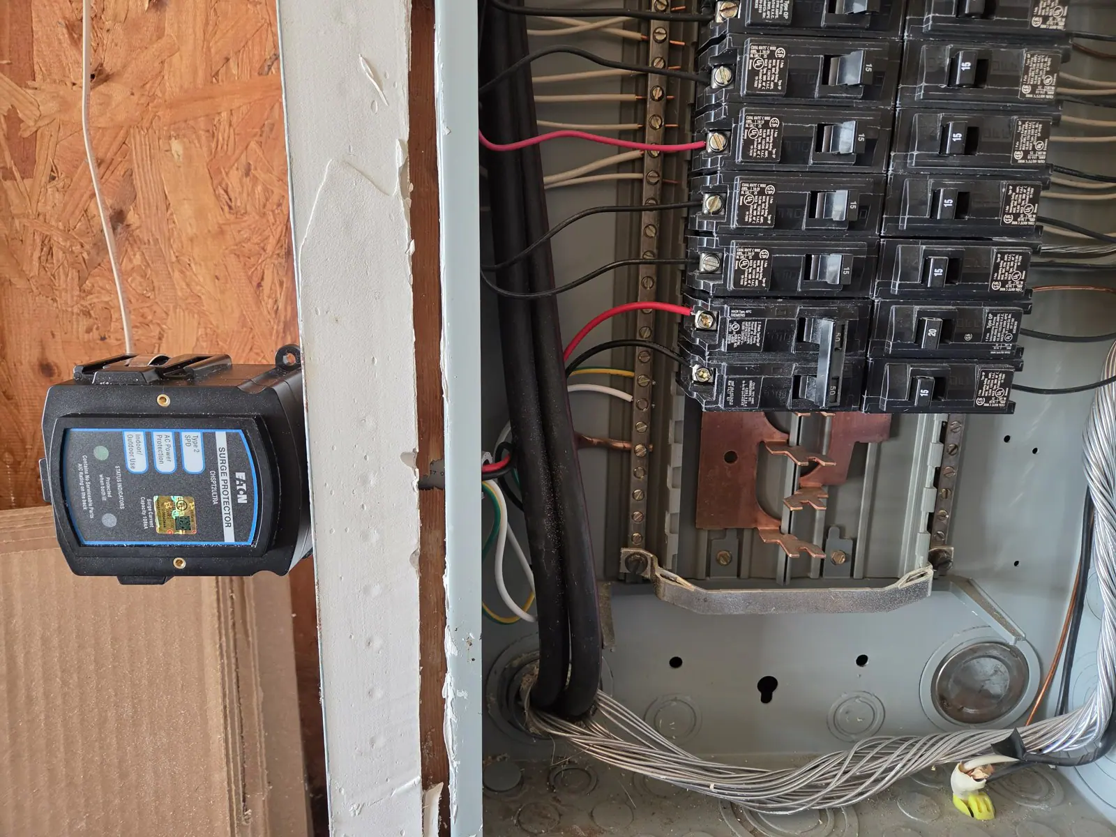 Surge protector mounted next to an open electrical panel showing breakers and wiring, in Wakefield, Raleigh