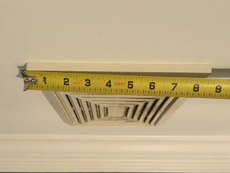 Tape measure across a bathroom ceiling vent to size the replacement