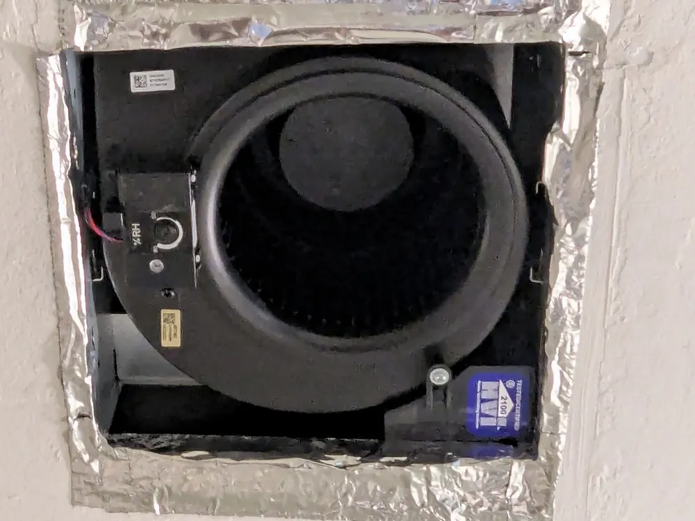 Bathroom exhaust fan housing mounted in the ceiling opening, sealed with foil tape