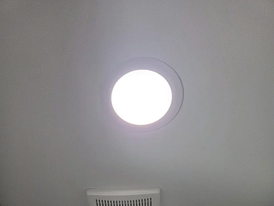 Round LED light glowing in a ceiling beside a bathroom vent