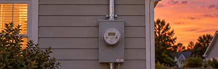 New electric meter base and service mast on the side of a house at dusk